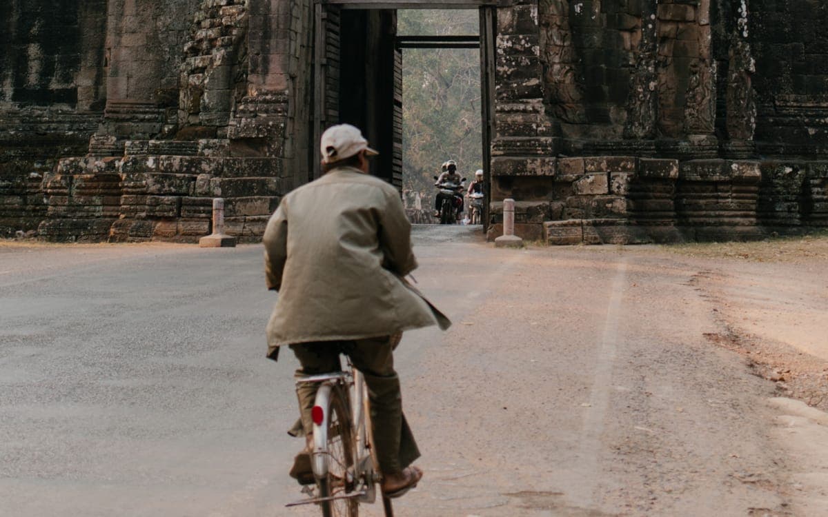 Woman in White Jacket Walking on Pathway Near Gray Concrete Building Cambodia